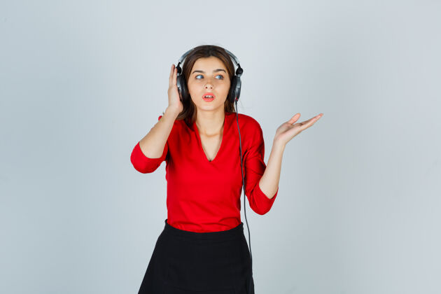 女性戴着耳机的年轻女士一边听音乐一边展示着穿红衬衫的东西笔记本电脑快乐倾听