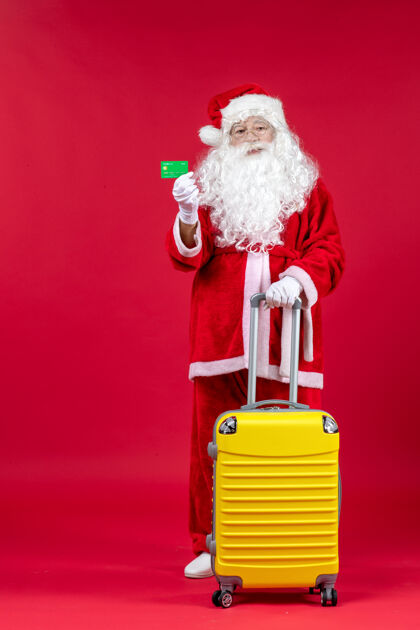 人红墙上挂着黄色袋子 手里拿着绿色银行卡的圣诞老人的正视图人们圣诞时尚