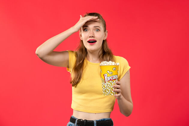 成人正面图年轻女子手捧爆米花包在浅红的墙上电影院看女孩电影女孩摆姿势封面