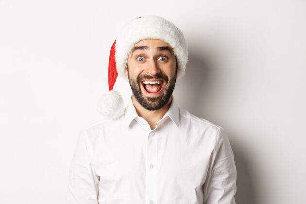 圣诞老人特写镜头：戴着圣诞帽的快乐胡须的家伙 看起来很惊讶 庆祝圣诞节 站着胡须快乐商人