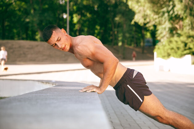 户外一位肌肉发达的男运动员在公园里锻炼身体体操 训练 健身 柔韧性锻炼夏日城市阳光明媚 生活方式积极健康 青春活力 健美人娱乐自然