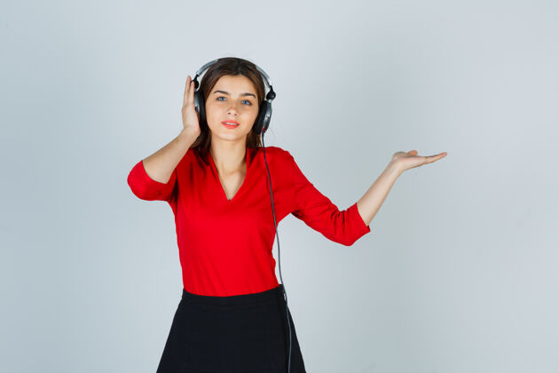 女人戴着耳机的年轻女士一边听音乐一边展示着穿红衬衫的东西展示女性成人