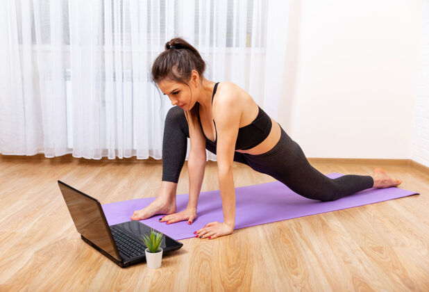 锻炼年轻的运动型女人在紫色的垫子上练习瑜伽 看着她的笔记本电脑女性健康普拉提
