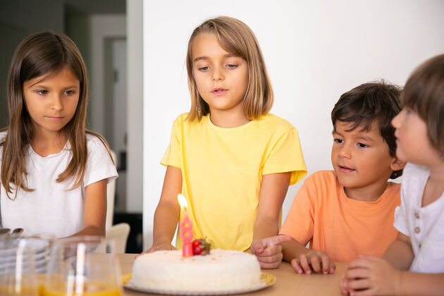 孩子可爱的金发女孩许下愿望 和朋友一起庆祝生日可爱的孩子们一起站在房间里 用蜡烛看着美味的蛋糕童年 庆祝和节日的概念站立男孩儿子