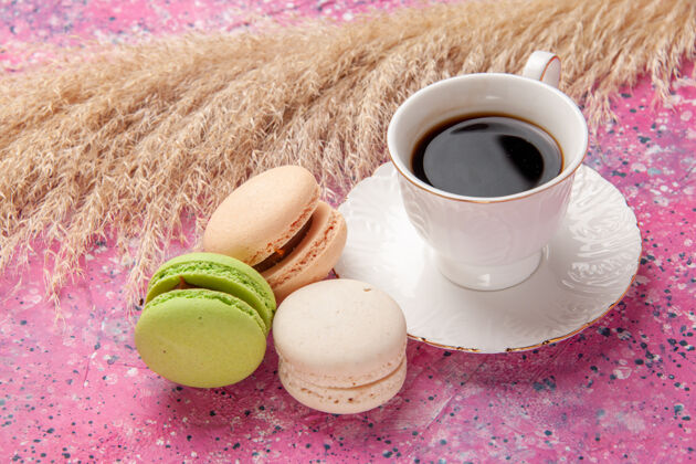 生的正面近距离观看法式马卡龙和一杯茶在粉红色的桌子上蛋糕糖甜甜的彩色派饼干麦卡龙饮料咖啡