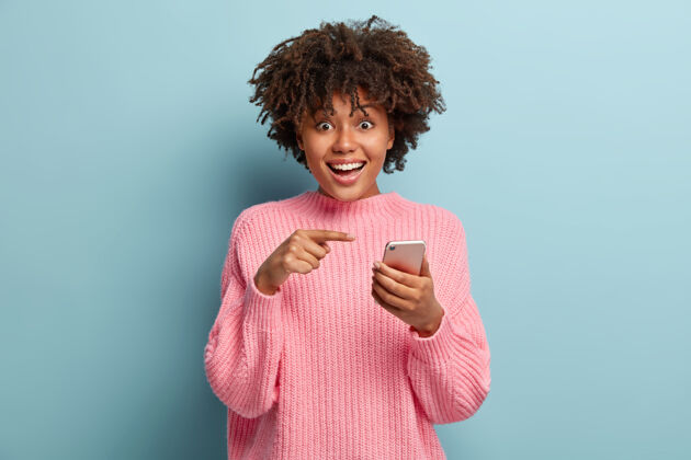 浏览惊讶的正黑皮肤女士指着智能手机设备 建议在群聊中交谈 邮箱里收到许多祝贺的短信 有喜出望外的样子高兴演示指向
