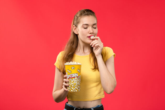 年轻女性正面图年轻女子在电影院拿着爆米花包 吃红墙电影剧院漂亮年轻人