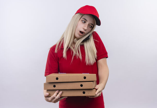 帽子一个穿着红色t恤和帽子的年轻女孩拿着比萨饼盒 在孤立的白色背景下讲电话T恤电话年轻