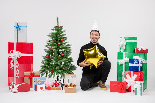 圣诞节年轻人围坐在礼物旁边 拿着金星在白色的墙上人盒子庆祝