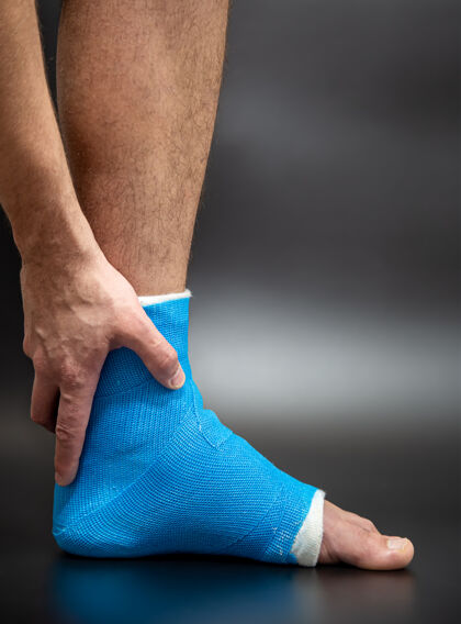 骨折蓝色夹板脚踝绷带腿上的男性病人投在黑暗模糊的背景运动损伤的概念闭合背景脚踝