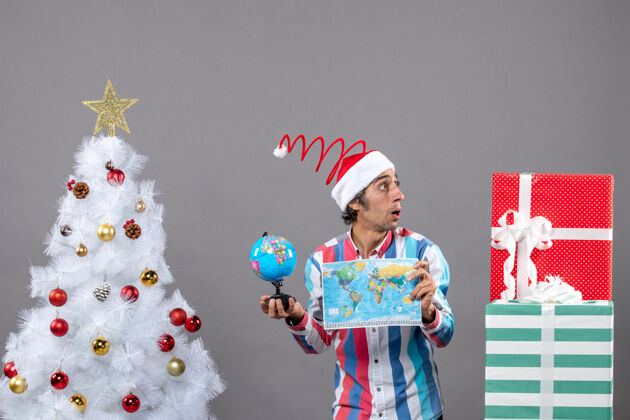 帽子正面图好奇的男子戴着螺旋弹簧圣诞帽看着礼物拿着世界地图和地球仪圣诞人好奇的人