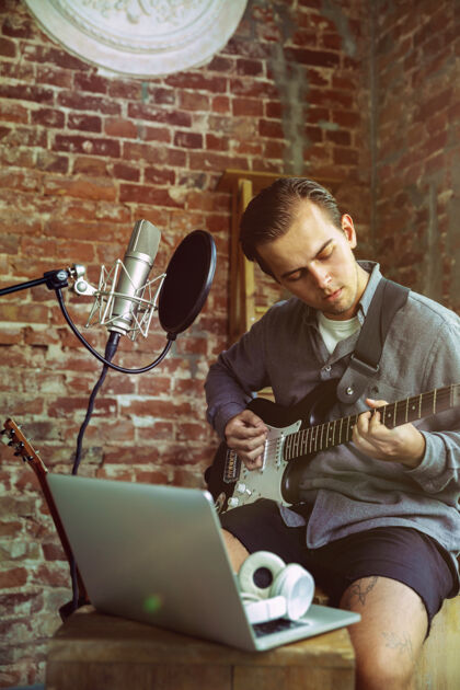 播放器年轻人坐在阁楼工作场所或家中录制音乐视频博客家教 弹吉他或制作广播网络教程爱好 音乐 艺术和创作的概念音乐视频男性