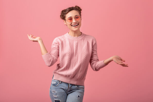 年轻年轻漂亮活泼的笑脸女郎 穿着粉色毛衣 戴着春日流行的太阳镜 以粉色工作室为背景粉色快乐女人