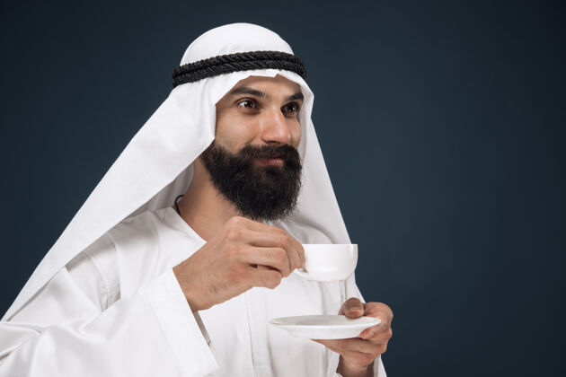反应阿拉伯沙特男子肖像年轻的男模站着喝咖啡或茶人男孩