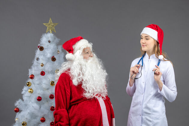 圣诞圣诞老人和年轻女医生在灰色墙壁上的正视图微笑节日圣诞快乐