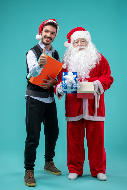 圣诞老人圣诞老人与年轻人和礼物在蓝色墙上的正面视图圣诞老人庆祝男性