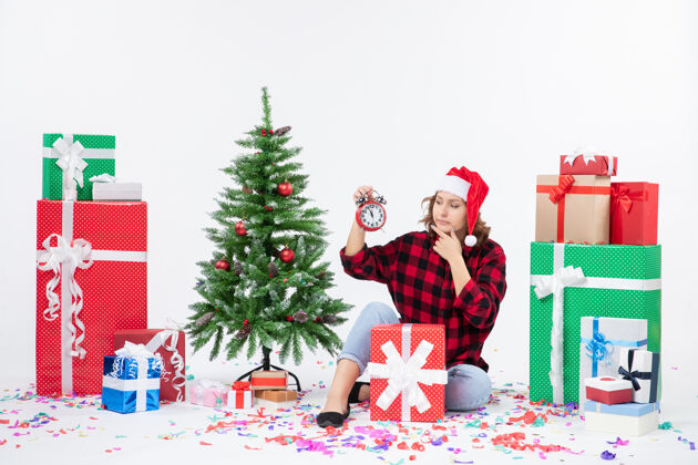前面前视图的年轻女子坐在圣诞礼物周围拿着白色墙上的时钟圣诞节情感圣诞快乐