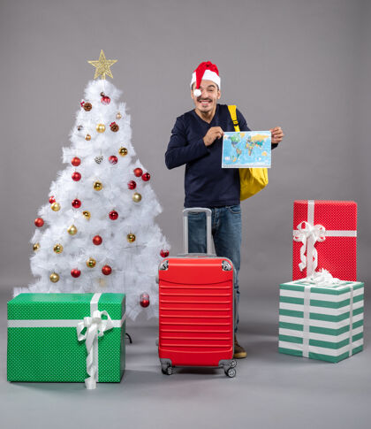 商店笑脸男拿着红色手提箱拿着地图双手放在灰色隔离带上圣诞帽圣诞树地图