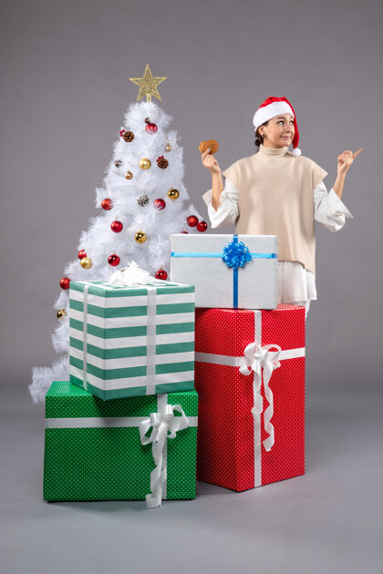 饼干在圣诞树旁的灰色地板上 年轻的女人拿着饼干和礼物女性圣诞老人礼物