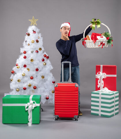盒子戴着圣诞帽的年轻人惊讶地看着圣诞树旁的礼品篮圣诞老人购物年轻