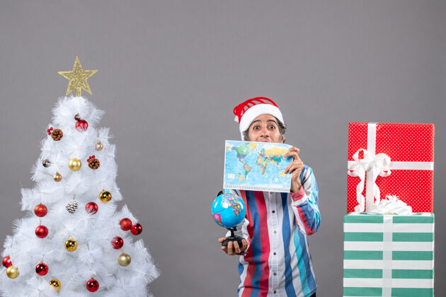 圣诞正面图快乐的男人用世界地图捂着脸拿着地球仪灰色礼品盒圣诞树