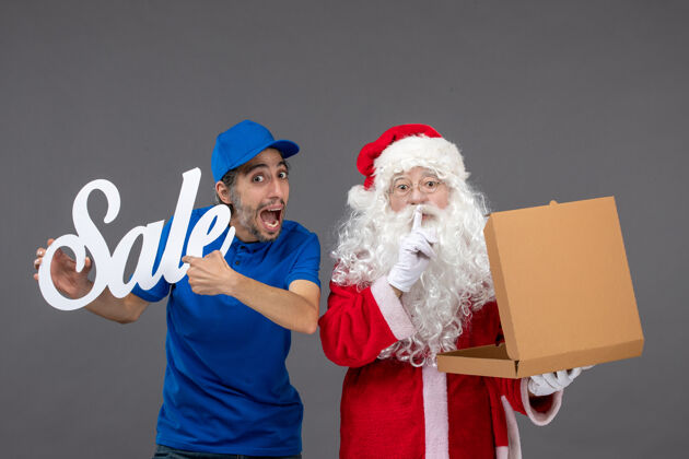 庆祝圣诞老人的正面图 男信使手持销售横幅 灰色墙上挂着食品盒圣诞老人人销售