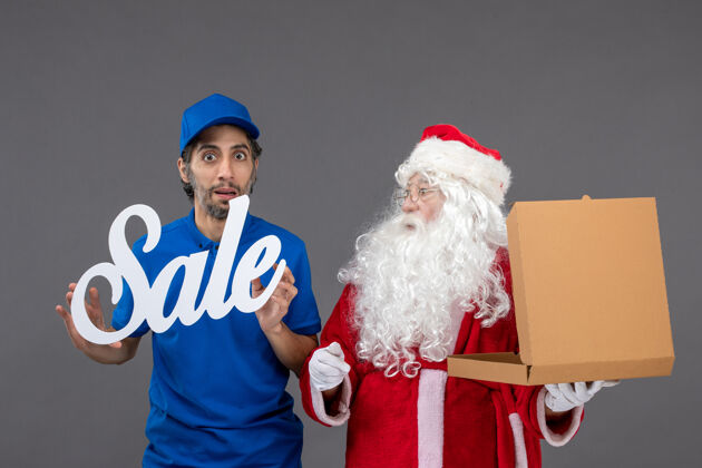庆祝圣诞老人的正面图 男性信使手持销售横幅 灰色墙上挂着食品盒举行节日帽子