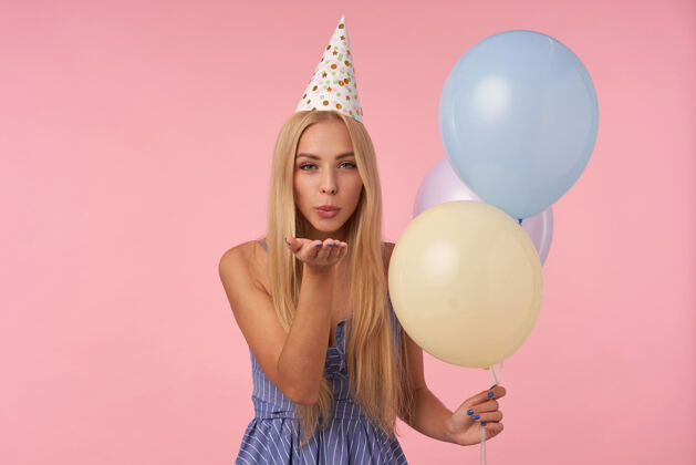 条纹美丽的年轻长发女子用五颜六色的气球庆祝生日 积极地看着相机 撅着嘴唇吹着飞吻头发亲吻摆姿势