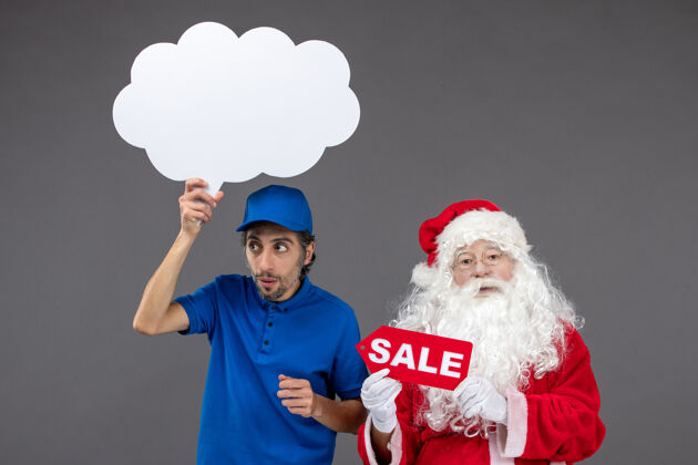 举行圣诞老人的正面图 男信使手持白云招牌和灰色墙上的销售横幅圣诞男帽子