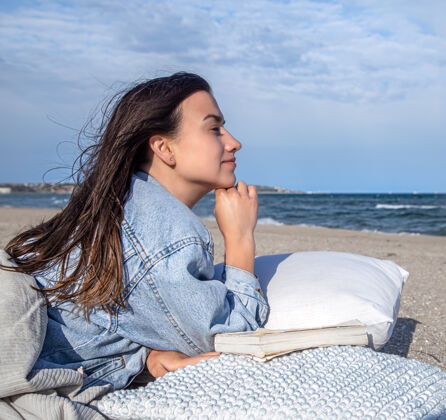 黑发放松的概念 一个女人在沙滩上 在有风的天气里 躺在枕头上看书女孩阅读夏天