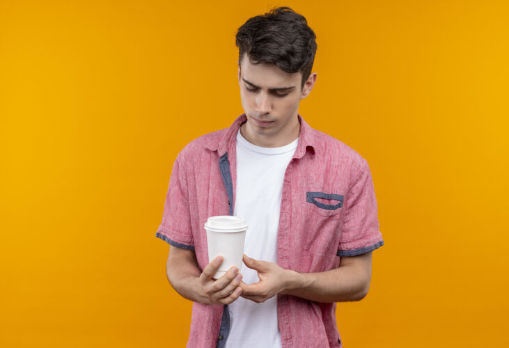 年轻悲伤的白人年轻人穿着粉色衬衫 在孤立的橙色背景上拿着一杯咖啡悲伤小伙子粉色