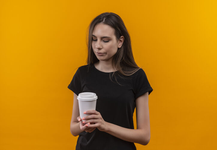 T恤悲伤的年轻白人女孩穿着黑色t恤看着咖啡杯孤立的橙色背景杯子女孩咖啡