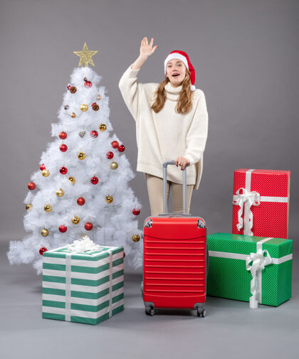 旅行者前视图欢呼圣诞女孩站在圣诞树和礼物附近行李美丽帽子