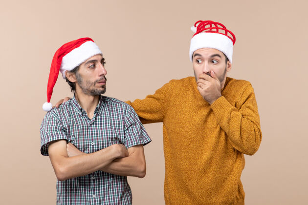 两个正面图两个戴着圣诞帽的男人 一个把手放在其他人的肩膀上 背景是米色的惊奇视图圣诞老人