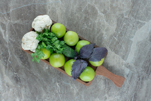 顶视图绿色的西红柿和花椰菜片 上面放着苋菜和欧芹叶 放在大理石托盘上未熟番茄蔬菜
