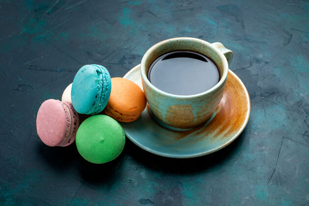 棕色前视图一杯茶 深蓝色背景上有法国马卡龙 烤蛋糕派 糖甜茶法式正面蓝色