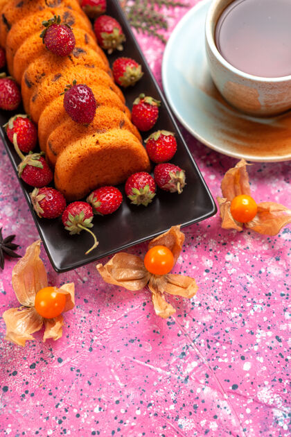 茶半顶视图美味的蛋糕放在黑色的蛋糕锅里 新鲜的红色草莓和一杯茶放在粉红色的桌子上红色饼干食物