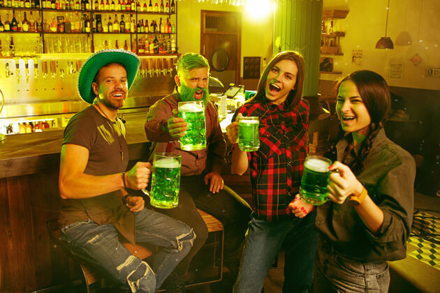 吐司圣帕特里克节聚会快乐的朋友们正在庆祝和喝绿色啤酒年轻男女戴着绿色帽子酒吧内部团体酒精酒吧