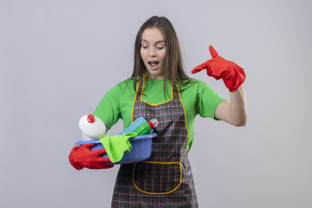 工具穿着红色手套制服的年轻女孩惊讶地指着她手上的清洁工具 背景是孤立的白色女孩年轻手套