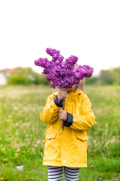 丁香一个穿着黄色夹克的小女孩用一束紫丁香遮住了她的脸春天乡村自然