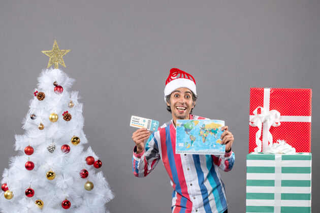 圣诞正面是戴着螺旋弹簧圣诞帽的快乐男人 手里拿着世界地图和旅行票地图假期快乐的人