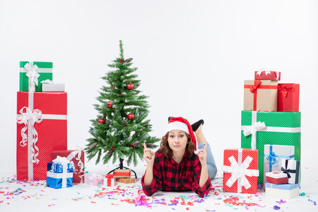 礼物正面图：年轻女性躺在圣诞礼物和白色背景上的小圣诞树上 新年女人圣诞雪精灵雪年轻冬青
