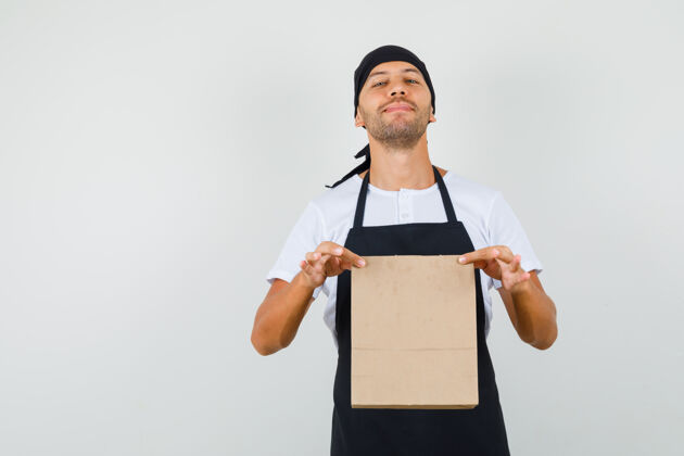 男人面包师穿着t恤 围裙 手里拿着纸袋 看上去很自豪前台男性厨师