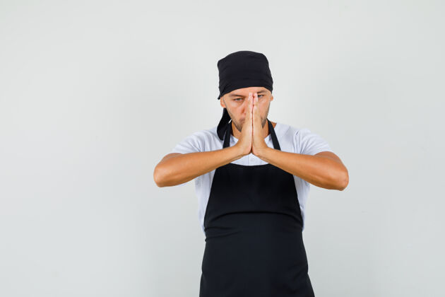 人面包师身穿t恤 围裙 手牵着手做祈祷的手势 看上去很平静年轻人成人烹饪