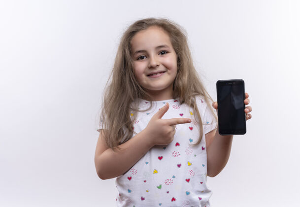 学校微笑的小女孩穿着白色t恤指着电话上孤立的白色背景白色电话点