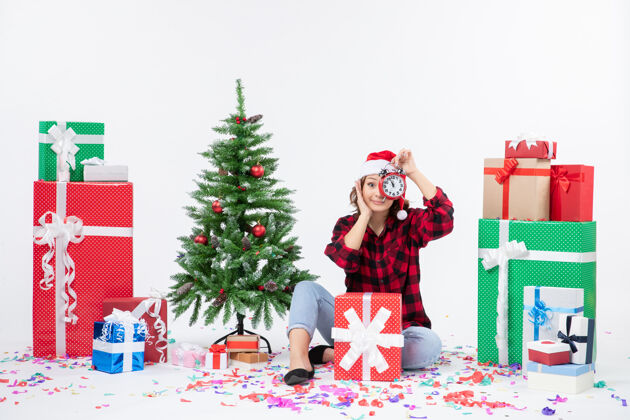 女人前视图的年轻女子坐在圣诞礼物周围拿着白色墙上的时钟时钟快乐人