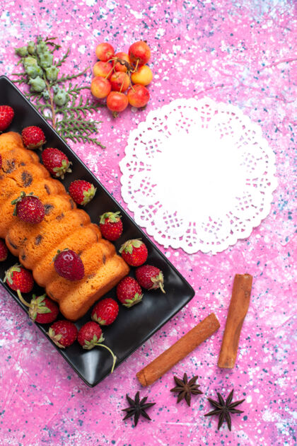 新鲜俯瞰美味的烤蛋糕在黑色的蛋糕锅里 粉红色的桌子上放着新鲜的红色草莓和肉桂糖水果黑色