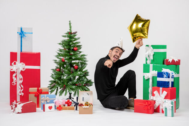 圣诞快乐正面图：年轻人围坐在礼物旁边 手里拿着白色墙上的金星礼物坐着明星