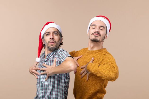 男人正面图：两个戴着圣诞帽的自信男人把手放在胸前 背景孤立视图前面男人