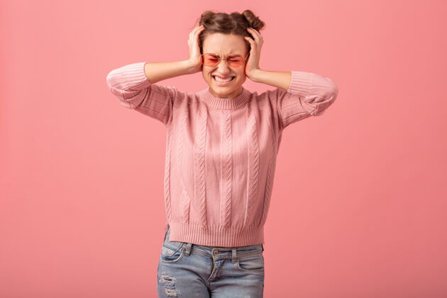 抑郁年轻漂亮有趣的女人有一个问题 感觉头痛 压力和举行她的头 在粉红色的毛衣和太阳镜孤立在粉红色的工作室背景痛苦疲倦女性
